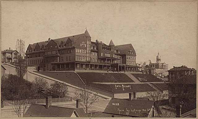 The Rainier Hotel sits atop a hill with stairs leading down to Fourth Avenue. It has two turrets and large bulk.